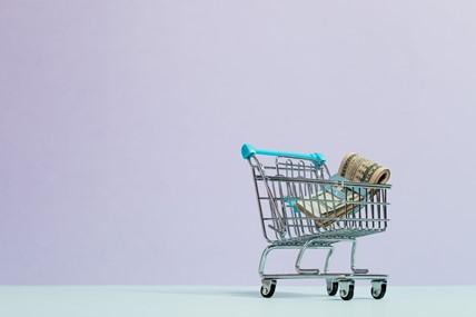 Klein winkelwagentje met opgerolde bankbiljetten tegen een lila achtergrond