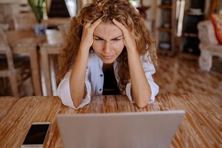 Vrouw met haar handen in het haar kijkt gestrest naar haar laptop aan een houten tafel